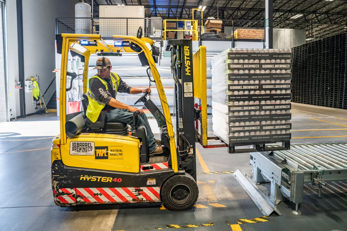 A forklift operator handling palletized cargo in an industrial warehouse.